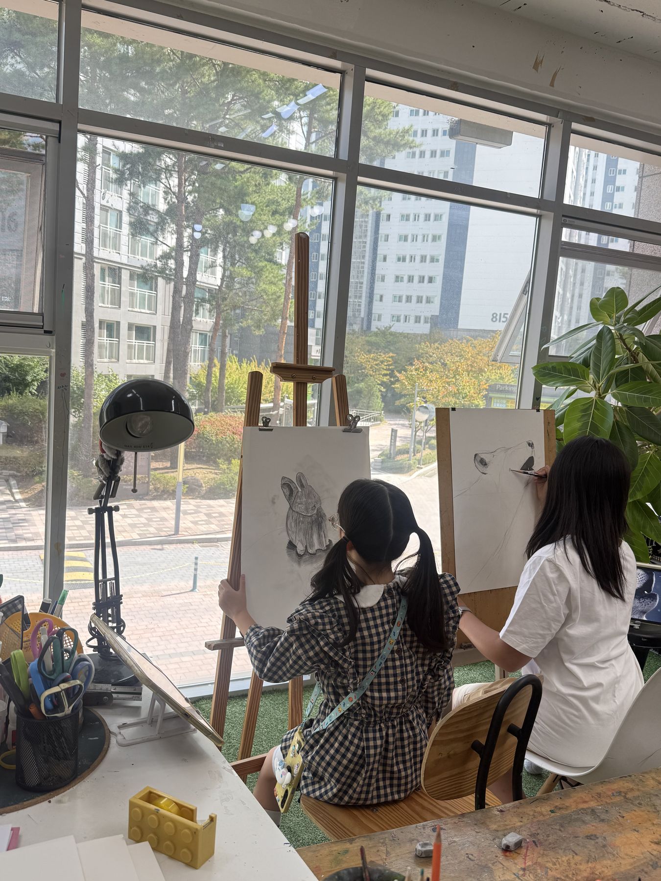 큰 창 앞 이젤에서 그림을 그리는 아이들